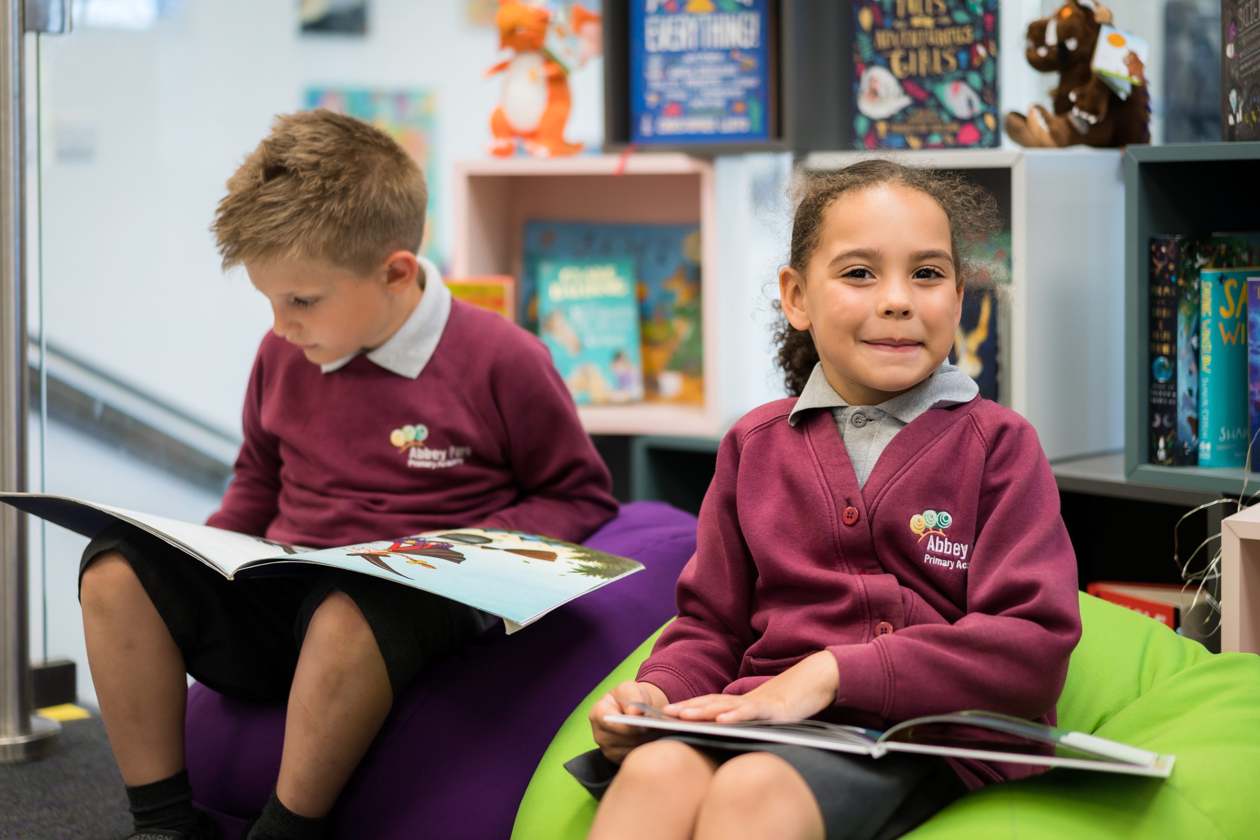Two children sit on a mat reading a book together.