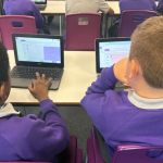 Image from behind of 2 students working on laptops.